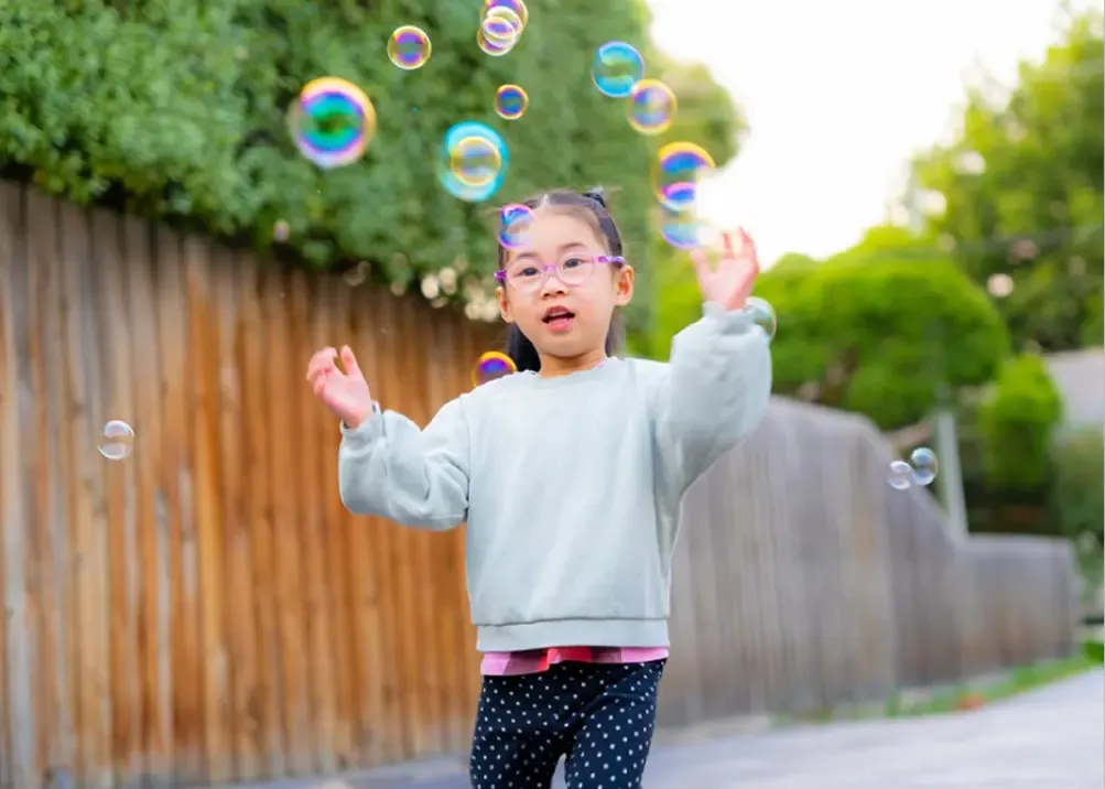 Ein Kind mit Brille, das draußen mit Seifenblasen spielt
